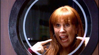 Donna Noble through a window, pointing to herself and grinning, from the series 4 opener