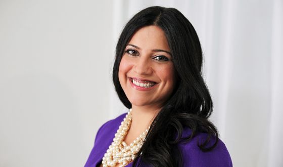 Reshma smiling, long black hair with purple jacket and pearls