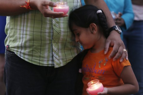 A young girl leans on a man, both holding candles during a vigil