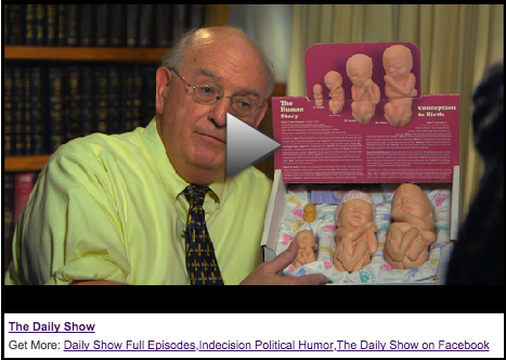 screenshot of man holding plastic fetus models