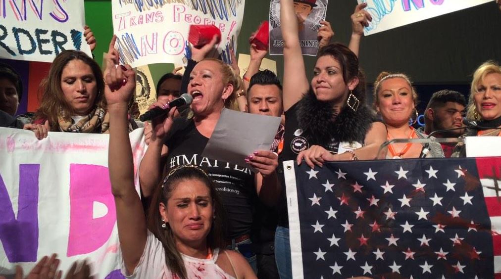Trans activist Bamby Salcedo on the mic surrounded by Trans WOC with fists up.