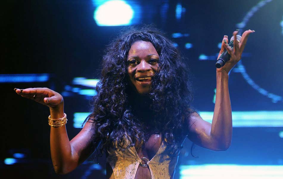 Black trans woman with long black hair raises her hands up on stage