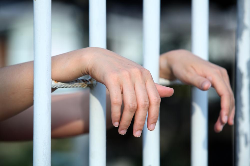 woman's hands behind bars