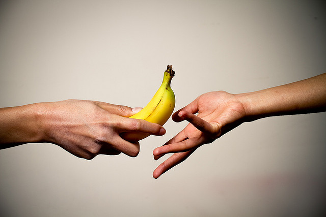 Image shows a person handing another person a banana.