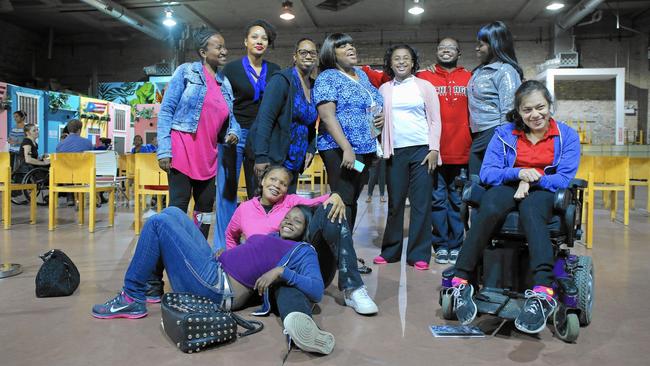 A group of young disabled women of color, some sitting, some standing, one in a powerchair.