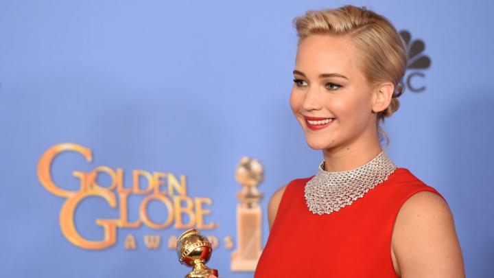 Jennifer Lawrence poses with a Golden Globe. She's wearing a floor length red dress and has her blonde hair back in a bun.