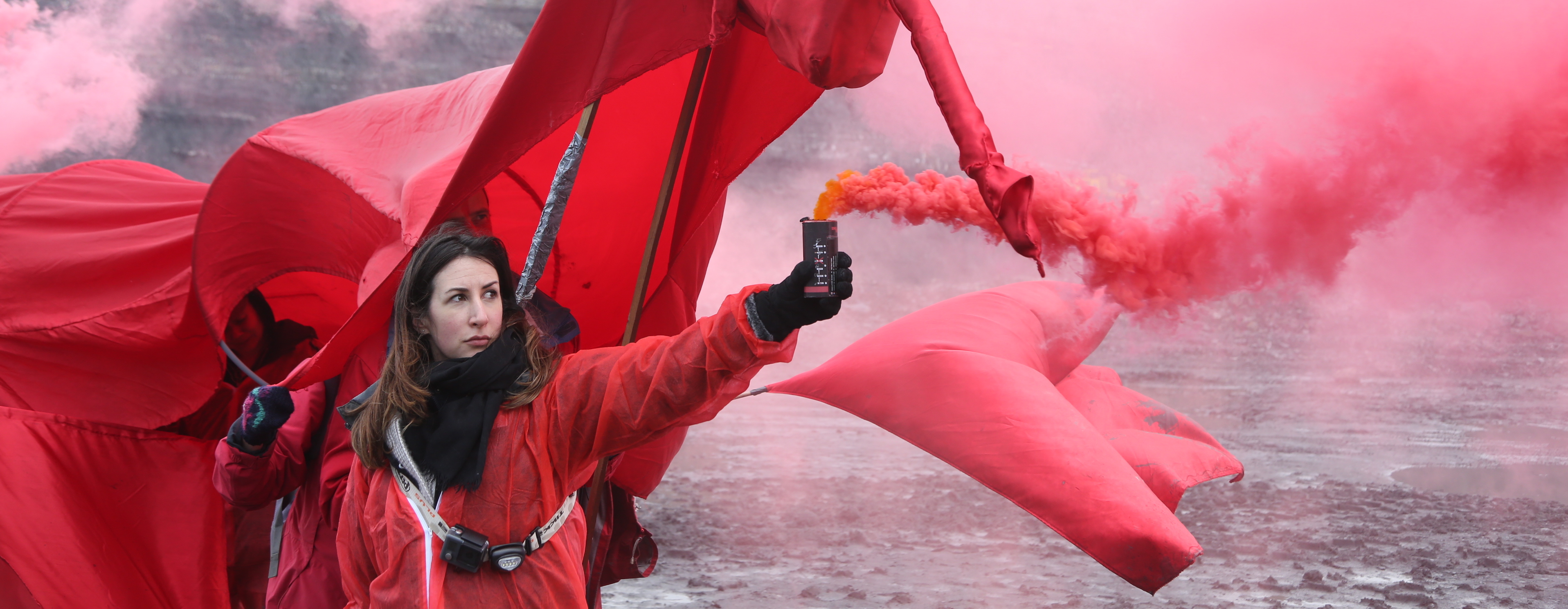 A woman dressed in red looses a canister of red smoke.