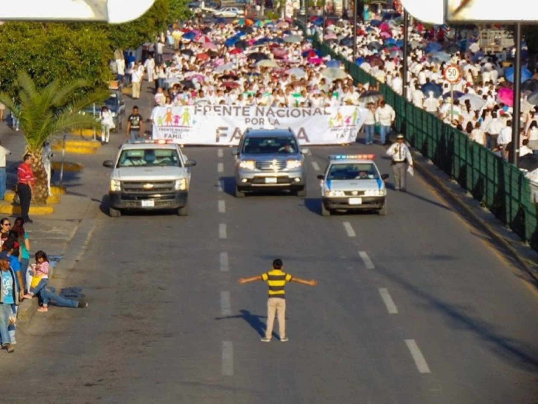 Boy stands in teh street in front of massive demonstration with arms open