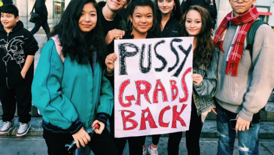 A group of people hold a sign saying "Pussy grabs back."