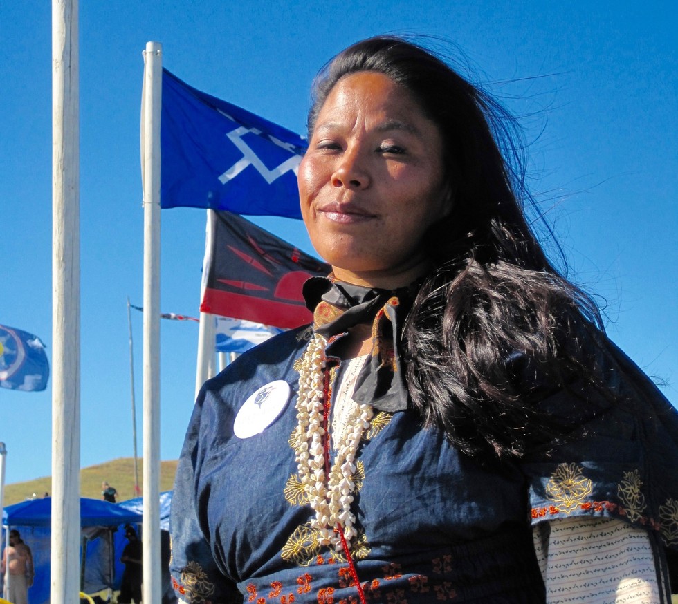 An Indigenous woman proudly stands against a bright blue sky.