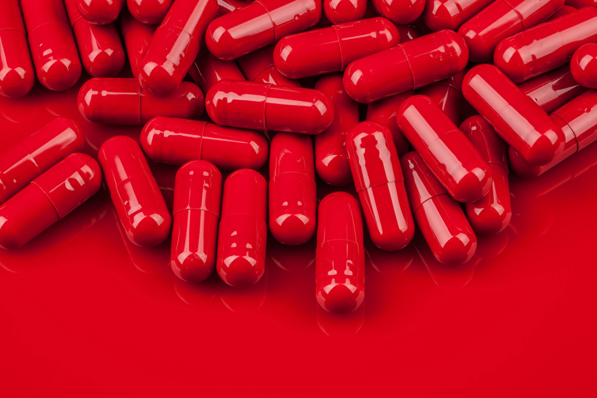 Macro photo of pile of red capsule pills on same color surface with copy space