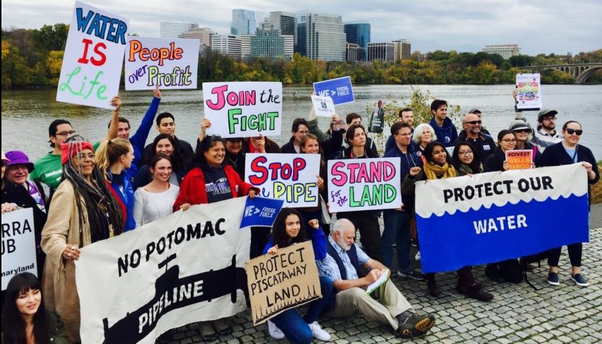 A group of activists hold signs near the potomac river protesting a proposed pipeline.