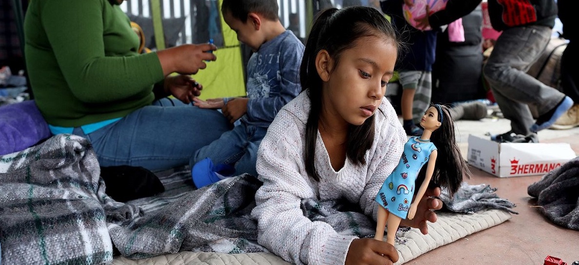 Young Latina girl sits in a tent, playing with a doll.